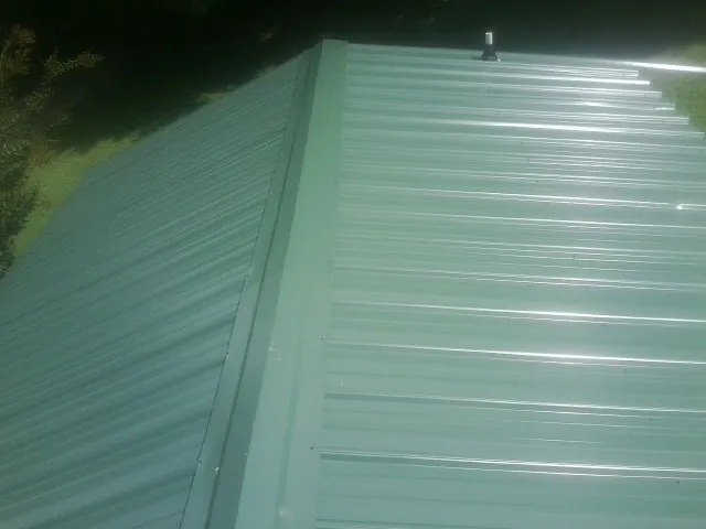 New green metal panels meeting at the ridge of a roof — Flat Roof Repair work by our crew in Jessup